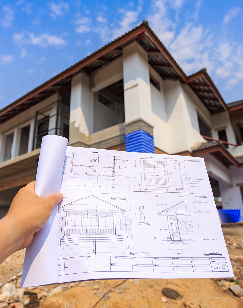 architecture drawings in hand in front of a new house construction site